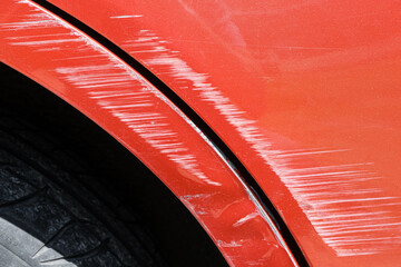 Close up of a red car with multiple visible scratches and paint damage The scratches expose the underlying metal, creating a contrast against the glossy surface. Perfect for automotive damage concepts