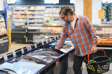 Bearded man with frozen fish his hands stands at the refrigerator in the department of frozen food