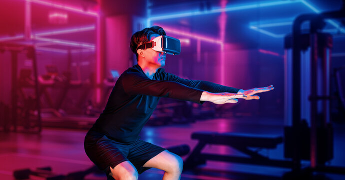 Asian man wearing VR glass while exercising at futuristic gym with glowing vibrant color. Male model using augmented reality technology for analysis data. Technology innovation concept. Ingenuity.