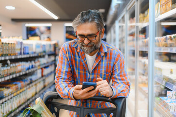 Senior man using mobile phone app while buying groceries in supermarket