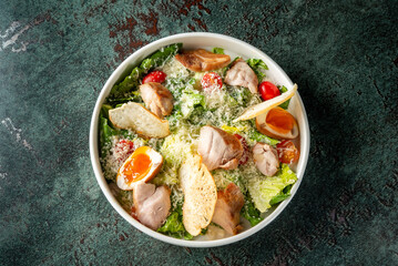 Fresh salad bowl featuring crisp romaine lettuce, cherry tomatoes, grilled chicken, croutons, and a soft-boiled egg, topped with grated cheese on a textured background.