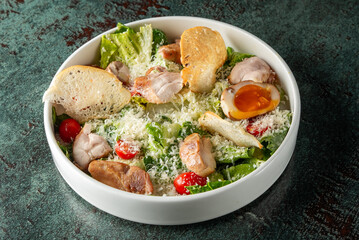 Fresh salad bowl featuring crisp romaine lettuce, cherry tomatoes, grilled chicken, croutons, and a soft-boiled egg, topped with grated cheese on a textured background.