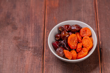 Dried dates and apricots in a bowl on a wooden table