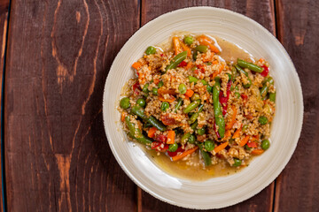 Couscous with vegetables in spices in a plate on a wooden table