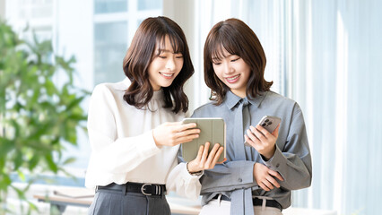 スマートフォンとタブレットを見て話す2人の女性・ビジネスウーマン