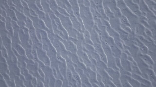 An aerial view of intricate snow formations on Glacier 3000 in the Swiss Alps. The wind has sculpted the snow into a mesmerizing pattern of parallel ridges and flowing textures. 