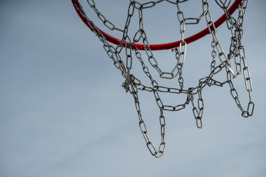 This detailed closeup image of a basketball hoop, featuring a shiny chain net contrasted against a vibrant blue sky, greatly enhances its overall visual appeal and attraction - Powered by Adobe