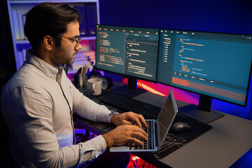 Smart IT developer working on laptop to type searching in software coding system at neon light...