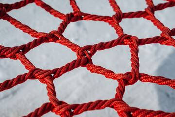 This is a closeup view of a vibrant red climbing net, complete with knots, situated on a playground surface designed for childrens adventures and safe exploration activities