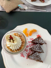 Dessert im Gläschen mit Sahne, Beerenmousse und Hafercrunch, auf einem Teller mit Gewürzkuchen in Tannenbaum Form serviert