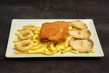 A plate of food with a piece of meat, french fries, and onion rings