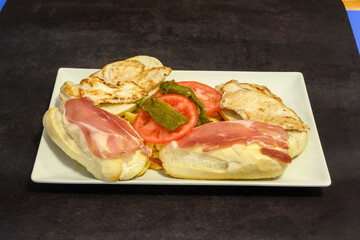 A plate of food with a sandwich, tomato, and ham