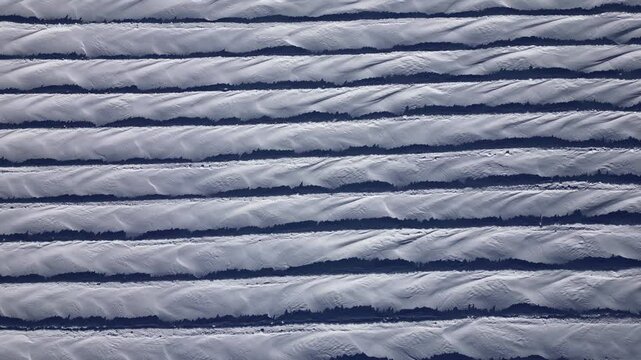 An aerial view of intricate snow formations on Glacier 3000 in the Swiss Alps. The wind has sculpted the snow into a mesmerizing pattern of parallel ridges and flowing textures. 