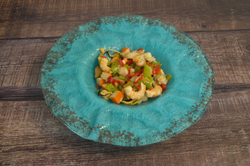 A blue plate with a variety of vegetables and shrimp