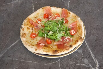 A pizza with ham, tomatoes, and spinach on top of a plate