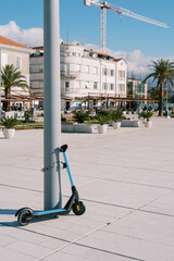 Rental electric scooter stands fastened to a pole on the promenade