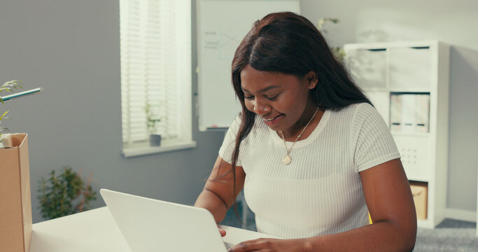 Beautiful woman secretary in company sits in office in front of laptop has break from work sends messages on social network to friend learns new rumors is shocked covers mouth with hand in disbelief