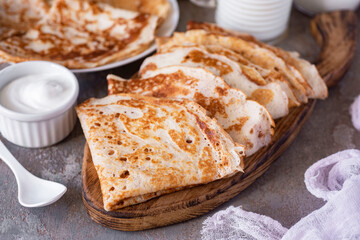 Delicious thin large pancakes for breakfast on a gray background for the whole family. Sweet pancakes on a wooden board. Close-up