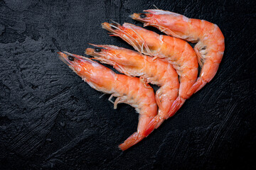 Four freshly cooked shrimps with brightly colored shells on a black textured background. Premium seafood.