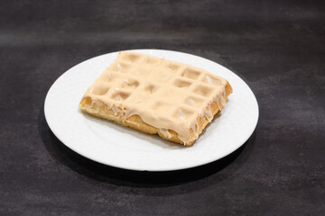 A waffle with a glaze on top sits on a white plate