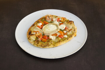 A pizza with cheese and tomatoes sits on a white plate