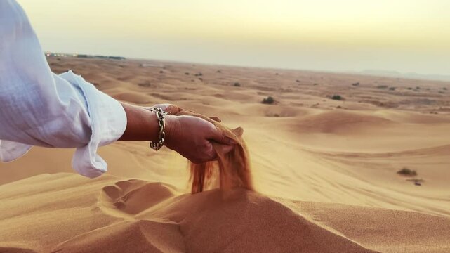 Woman spiling sand pouring in slow motion in sunset desert landscape in the United Arab Emirates