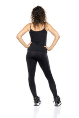 Rear view of young woman with curly hair wearing black tank top and leggings, showing athletic outfit from behind while standing against white background