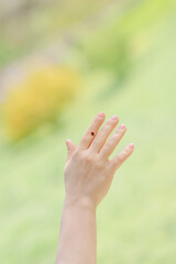 Hand with a ladybug on a finger on a blurred green backdrop.