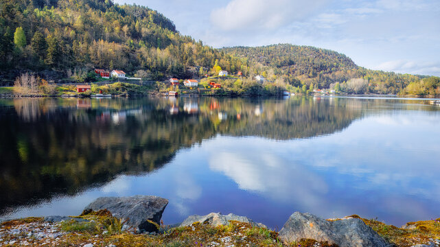 Bright wooden cottages reflecting in tranquil lake, green forested hills. Picturesque reflections of nature and houses, nordic countryside. For eco-tourism guides and lifestyle blogs. Copy space