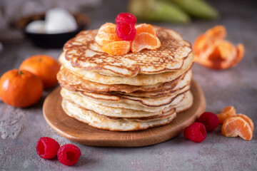 A stack of thin large pancakes for breakfast on a gray background. Thin large pancakes with pieces of fruit for dessert.Close-up