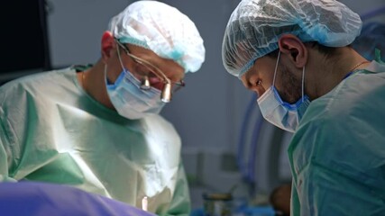 Professional male surgeons perform operation in cooperation. Main doctor wearing surgical loupes at surgery.