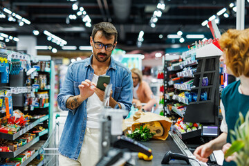 Customer using smartphone while shopping at checkout in supermarket