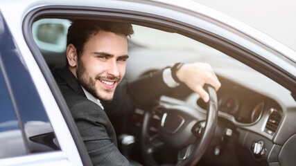 Handsome smiling entrepreneur sitting on driver's seat of his car in city