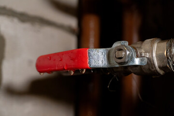 Close-up of red metal valve handle with water droplets on industrial pipe