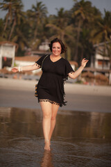 A beautiful fat girl in a summer Indian sundress walks along the sandy shore of the ocean