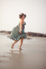 A beautiful fat girl in a summer Indian sundress walks along the sandy shore of the ocean