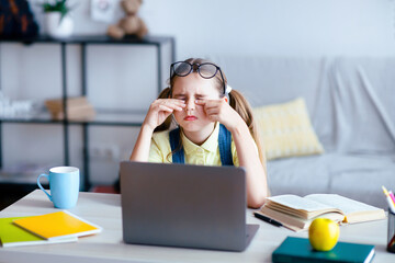 Eyes Fatigue. Tired little teenage girl feeling eyestrain, rubbing dry irritated eyes, sitting at...