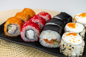 Colorful sushi variety with roll selection on black plate