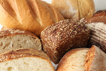 Whole and cut bread loafs on white table, closeup