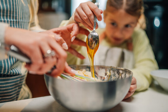 Mother and daughter adding honey to cake batter in mixing bowl