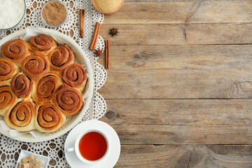 Freshly baked cinnamon rolls, tea and spices on wooden table, flat lay. Space for text