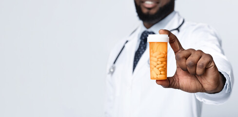 Cropped view of african american male doctor in white uniform with pill bottle on white studio background
