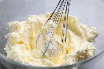 Bowl with whisk and whipped cream on grey table, closeup