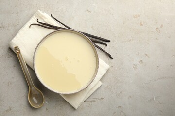 Tasty condensed milk, spoon and vanilla pods on light grey table, flat lay. Space for text