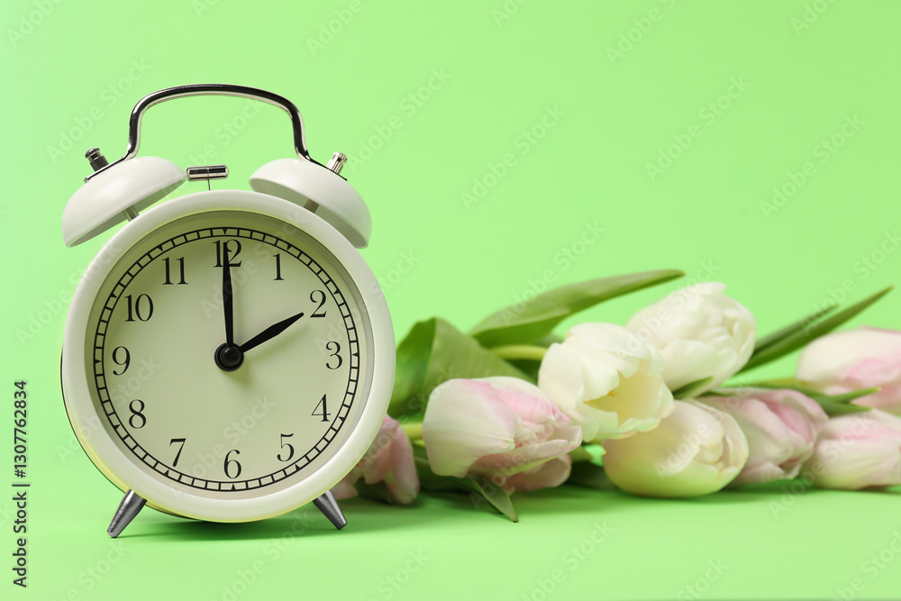Poster spring time. alarm clock and beautiful tulips on green background