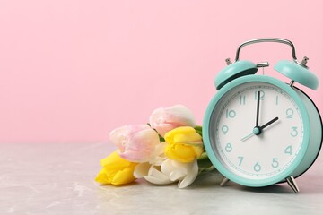 Spring time. Alarm clock and beautiful tulips on grey marble table against pink background, space...