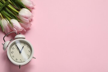 Spring time. Alarm clock and beautiful tulips on pink background, flat lay. Space for text