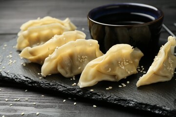 Tasty boiled gyoza (dumplings) with soy sauce and sesame on black wooden table, closeup