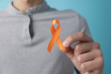 Multiple Sclerosis awareness. Man with orange ribbon on light blue background, closeup