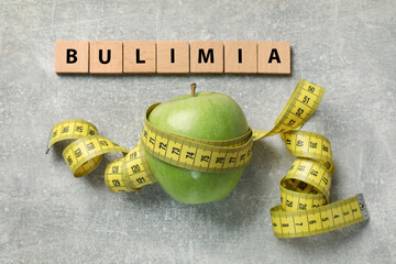 Squares with word Bulimia, green apple and measuring tape on grey table, flat lay
